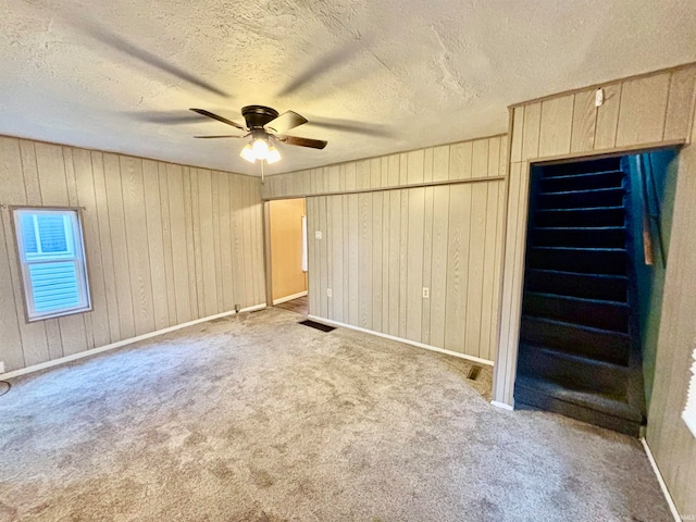 interior space featuring carpet flooring, ceiling fan, a textured ceiling, and wood walls