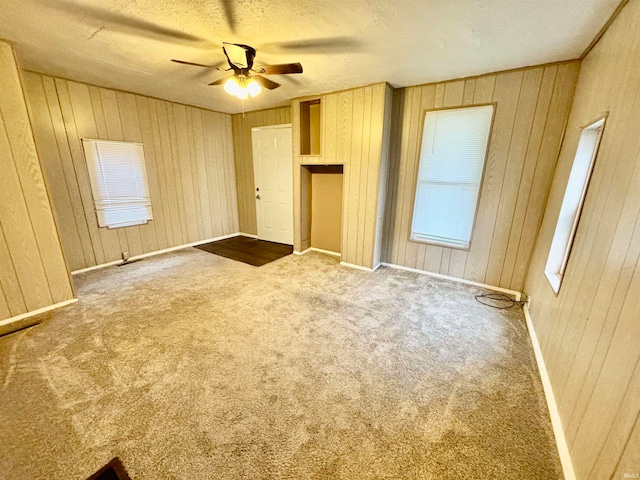 interior space with carpet flooring, a textured ceiling, ceiling fan, and wooden walls