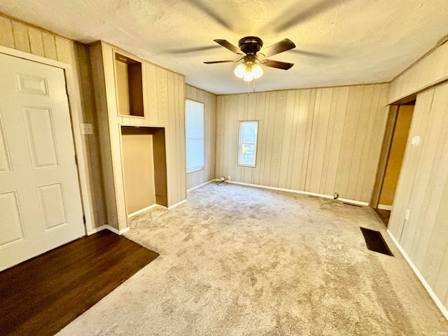 unfurnished bedroom featuring ceiling fan, wood walls, carpet floors, and a textured ceiling