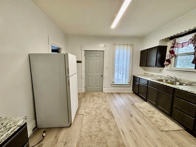 kitchen featuring light stone counters, light hardwood / wood-style floors, dark brown cabinets, sink, and white fridge