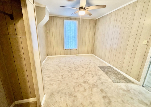 carpeted empty room featuring crown molding, ceiling fan, and wood walls