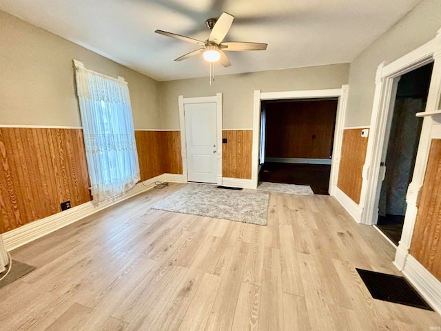 unfurnished bedroom with light hardwood / wood-style flooring, ceiling fan, and wood walls