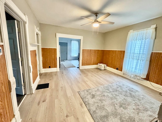 unfurnished room with a wealth of natural light, wooden walls, ceiling fan, and light hardwood / wood-style floors