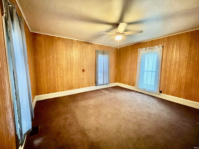 carpeted empty room with ceiling fan and wood walls