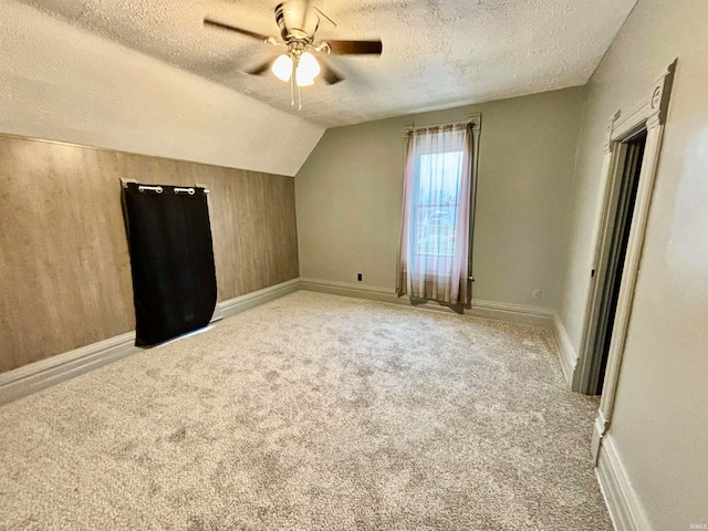 additional living space with ceiling fan, light colored carpet, lofted ceiling, a textured ceiling, and wooden walls