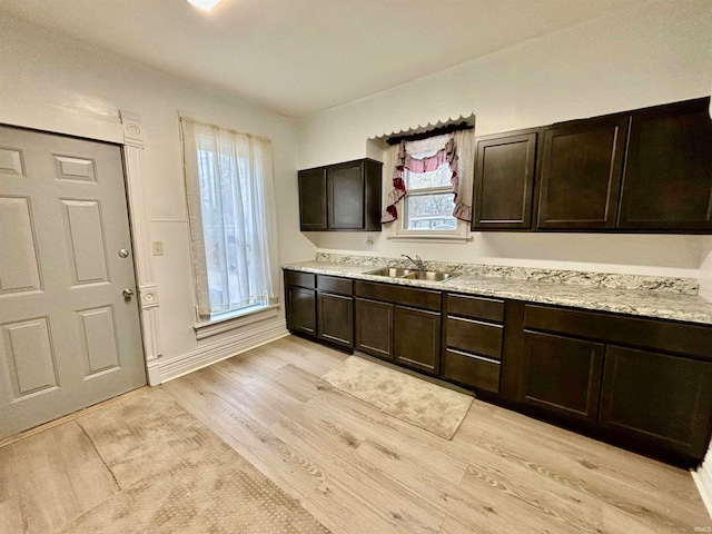 kitchen featuring light stone counters, dark brown cabinets, light hardwood / wood-style floors, and sink