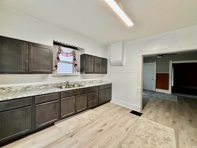 kitchen featuring dark brown cabinets, light stone counters, sink, and light hardwood / wood-style flooring