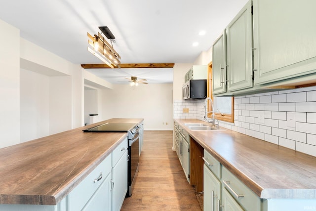 kitchen with light wood-type flooring, backsplash, stainless steel appliances, sink, and green cabinetry