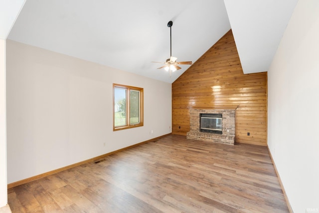 unfurnished living room with light wood-type flooring, vaulted ceiling, ceiling fan, wooden walls, and a fireplace