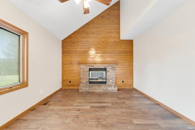 unfurnished living room with lofted ceiling, wood walls, light wood-type flooring, and a brick fireplace