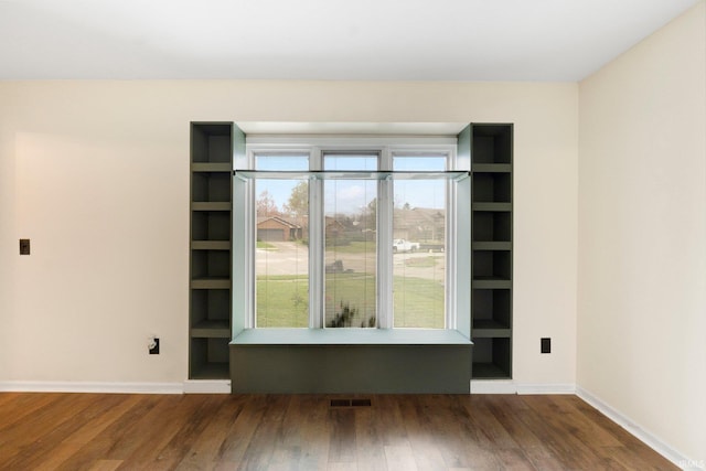 empty room with built in shelves and dark wood-type flooring