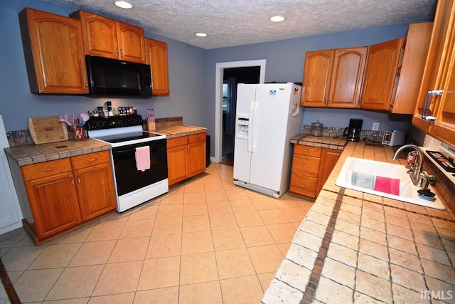 kitchen featuring a textured ceiling, white appliances, sink, light tile patterned floors, and tile counters