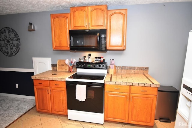 kitchen with a textured ceiling, tile countertops, white electric stove, and light tile patterned flooring