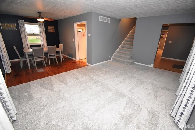 unfurnished living room featuring dark colored carpet, a textured ceiling, and ceiling fan