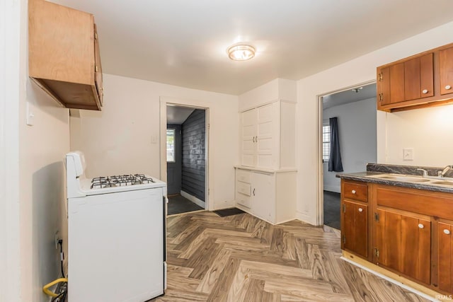 kitchen with white range with gas stovetop, sink, a wealth of natural light, and light parquet flooring