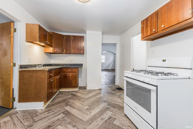 kitchen featuring white gas stove, sink, and light parquet flooring