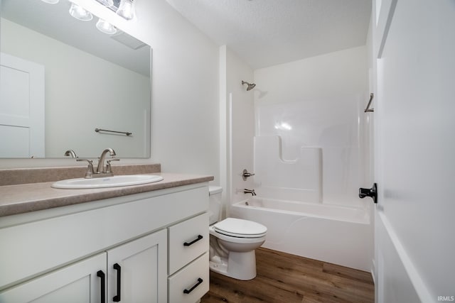 full bathroom featuring washtub / shower combination, hardwood / wood-style floors, a textured ceiling, toilet, and vanity