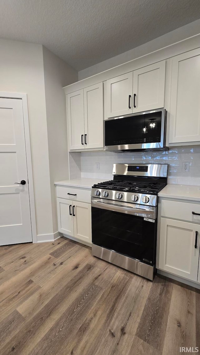 kitchen with appliances with stainless steel finishes, tasteful backsplash, white cabinetry, and light hardwood / wood-style floors