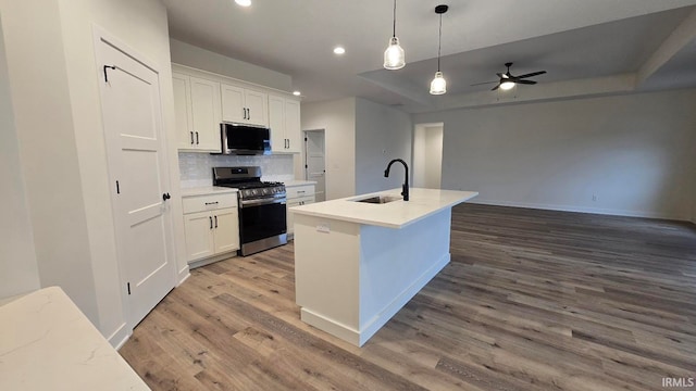 kitchen with stainless steel range, a tray ceiling, a kitchen island with sink, sink, and white cabinets