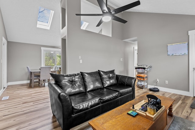 living room featuring light wood-type flooring, a skylight, high vaulted ceiling, and ceiling fan