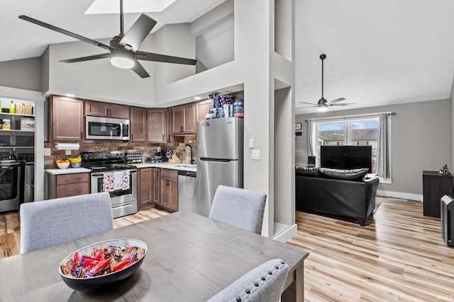 kitchen featuring washer and clothes dryer, high vaulted ceiling, sink, light wood-type flooring, and stainless steel appliances