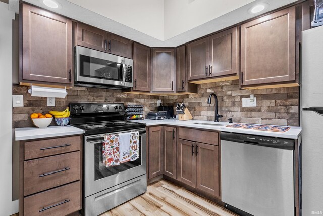 kitchen with sink, tasteful backsplash, dark brown cabinets, light hardwood / wood-style floors, and stainless steel appliances