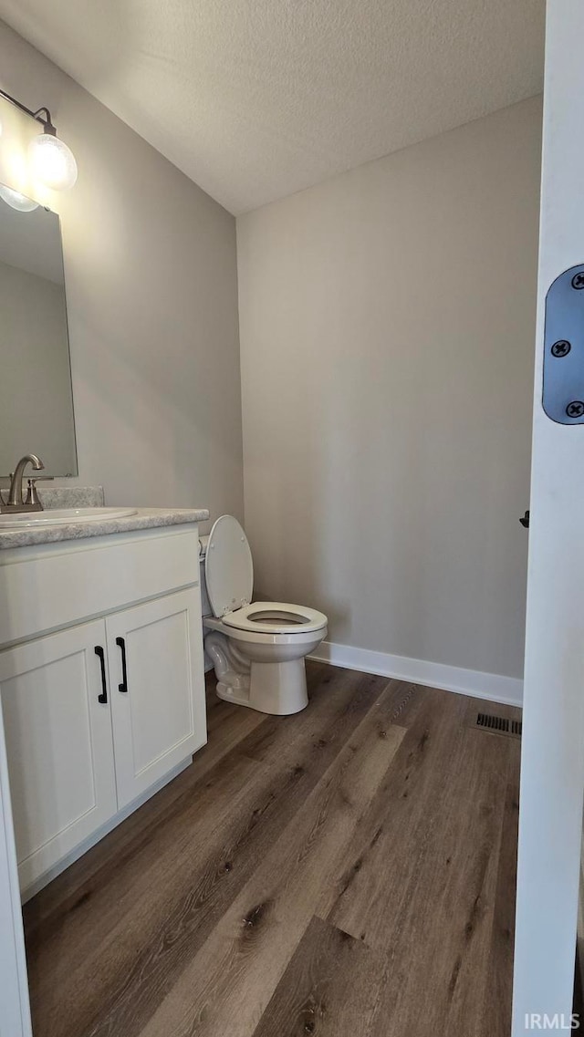 bathroom with hardwood / wood-style flooring, vanity, toilet, and a textured ceiling