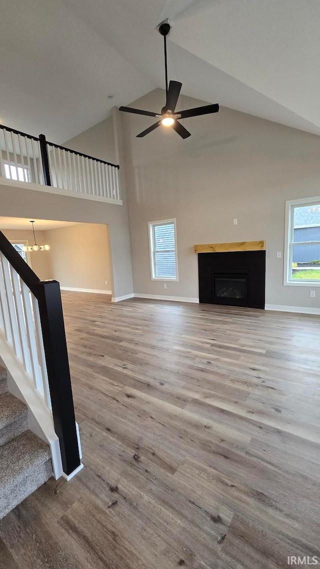 unfurnished living room with hardwood / wood-style flooring, ceiling fan with notable chandelier, a wealth of natural light, and high vaulted ceiling