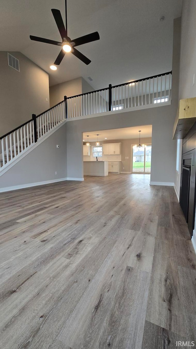 unfurnished living room with ceiling fan with notable chandelier, light wood-type flooring, and high vaulted ceiling