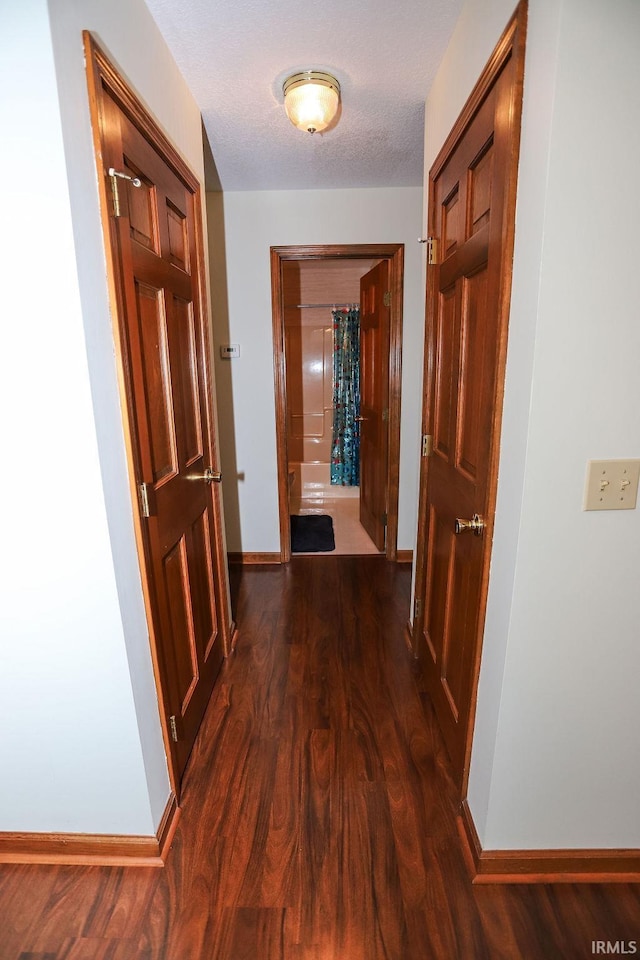 corridor with a textured ceiling and dark hardwood / wood-style floors