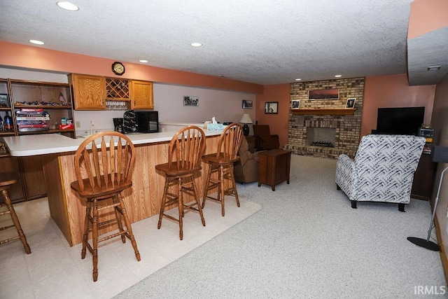 interior space with a breakfast bar area, kitchen peninsula, a fireplace, and a textured ceiling