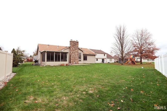 rear view of property featuring a sunroom, central AC unit, a playground, and a yard