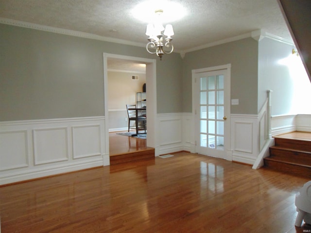 unfurnished dining area featuring hardwood / wood-style floors, a notable chandelier, ornamental molding, and a textured ceiling