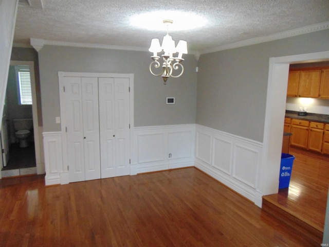 unfurnished dining area featuring a textured ceiling, dark hardwood / wood-style floors, crown molding, and a chandelier