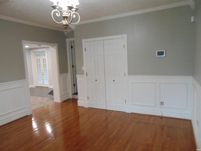 unfurnished bedroom featuring a chandelier, hardwood / wood-style flooring, a closet, and crown molding