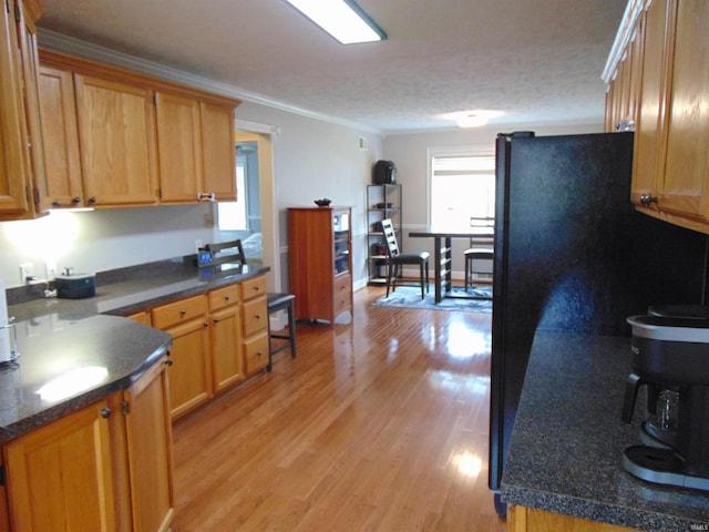 kitchen featuring light hardwood / wood-style floors, black refrigerator, ornamental molding, and a textured ceiling