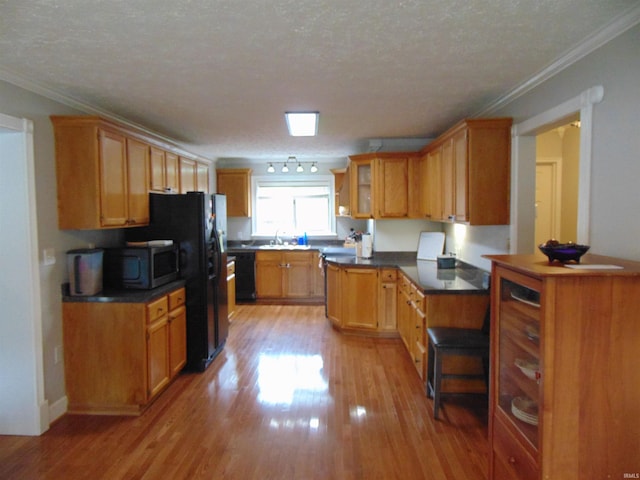 kitchen featuring sink, light hardwood / wood-style flooring, ornamental molding, black dishwasher, and a textured ceiling