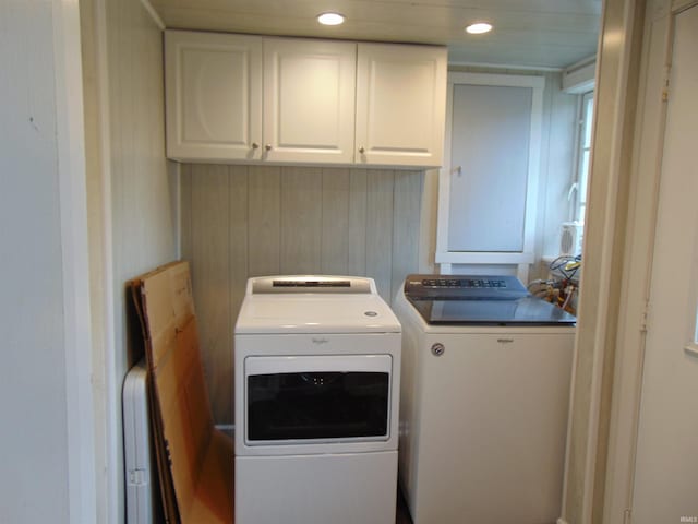 clothes washing area with cabinets, washer and clothes dryer, and wood walls