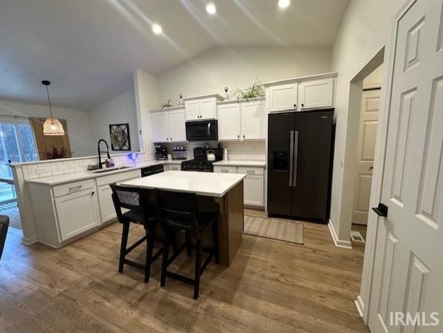 kitchen with sink, kitchen peninsula, pendant lighting, vaulted ceiling, and black appliances