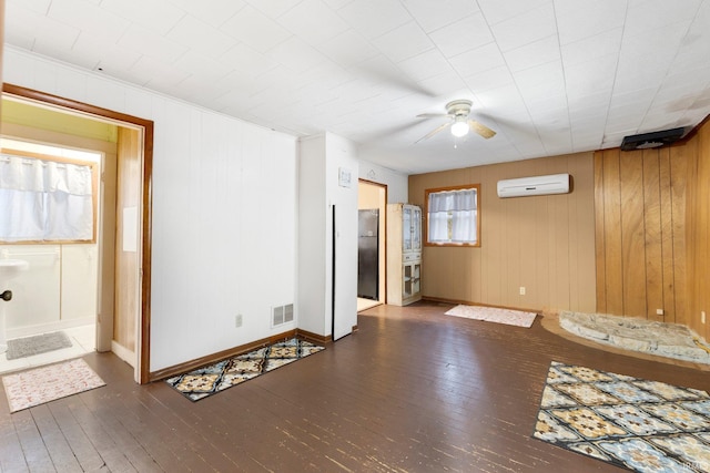 empty room with ceiling fan, an AC wall unit, dark wood-type flooring, and wooden walls