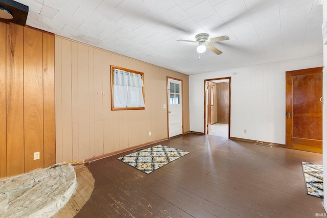 empty room featuring dark hardwood / wood-style flooring, ceiling fan, and wood walls