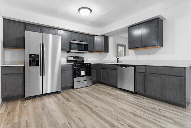 kitchen featuring light stone counters, a textured ceiling, stainless steel appliances, sink, and light hardwood / wood-style flooring