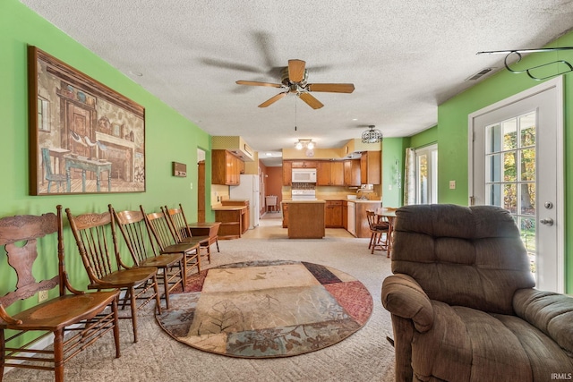 living room with ceiling fan, a textured ceiling, and light carpet