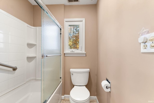 bathroom featuring toilet, shower / bath combination with glass door, and a textured ceiling