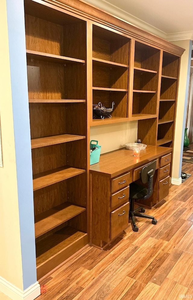 unfurnished office featuring built in desk, ornamental molding, and light hardwood / wood-style flooring