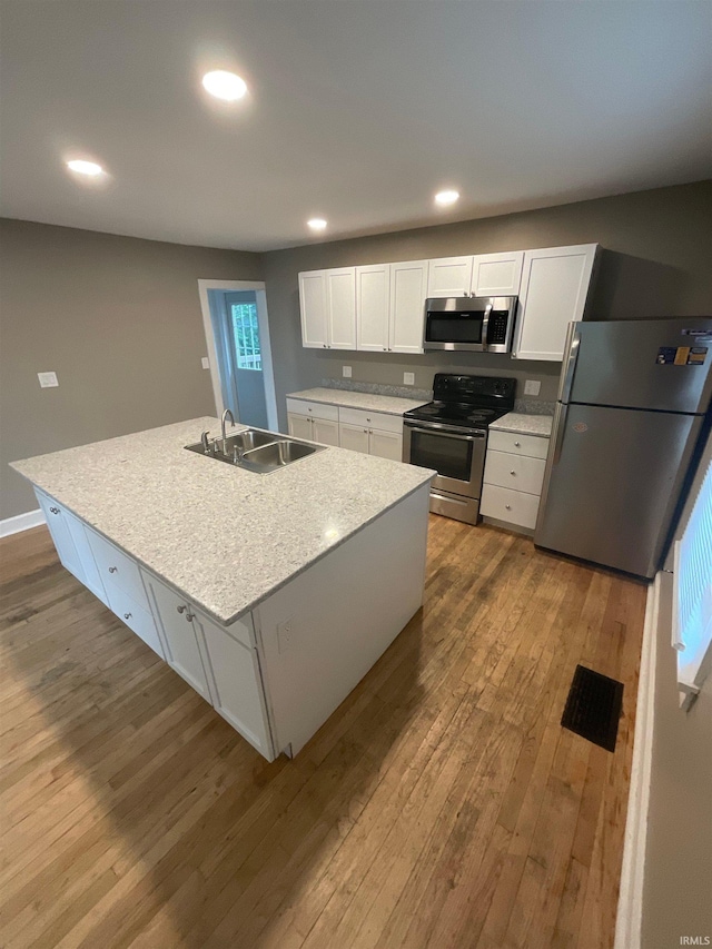 kitchen with white cabinets, appliances with stainless steel finishes, a kitchen island with sink, and sink