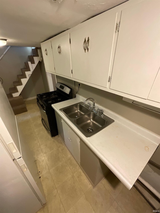 kitchen with sink, light tile patterned floors, stainless steel range with gas cooktop, refrigerator, and white cabinets