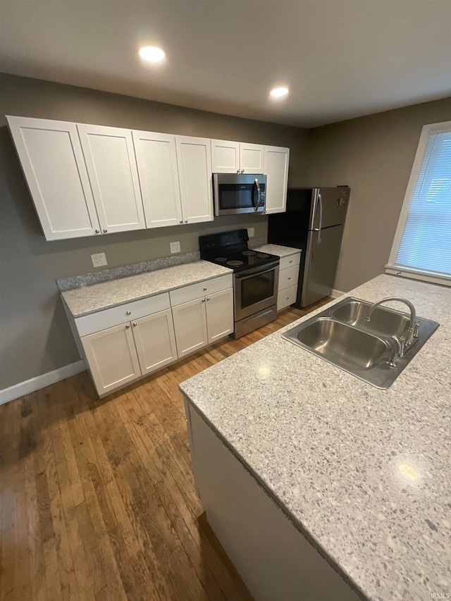 kitchen with hardwood / wood-style floors, white cabinets, sink, and stainless steel appliances