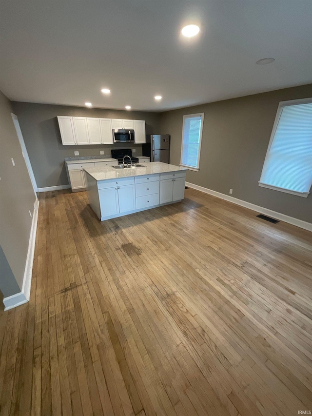 kitchen featuring light wood-type flooring, stainless steel appliances, a kitchen island with sink, sink, and white cabinetry