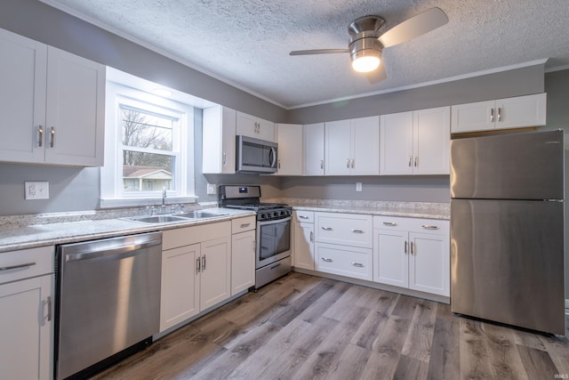 kitchen with stainless steel appliances, ceiling fan, sink, white cabinets, and light hardwood / wood-style floors